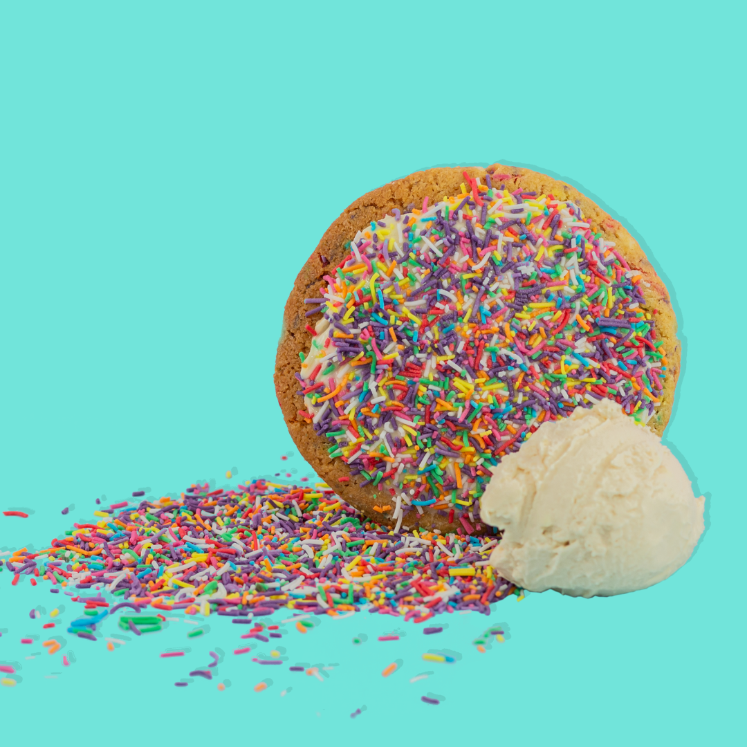 Cake Batter Maxi cookie with vibrant rainbow sprinkles and creamy frosting on a blue background.