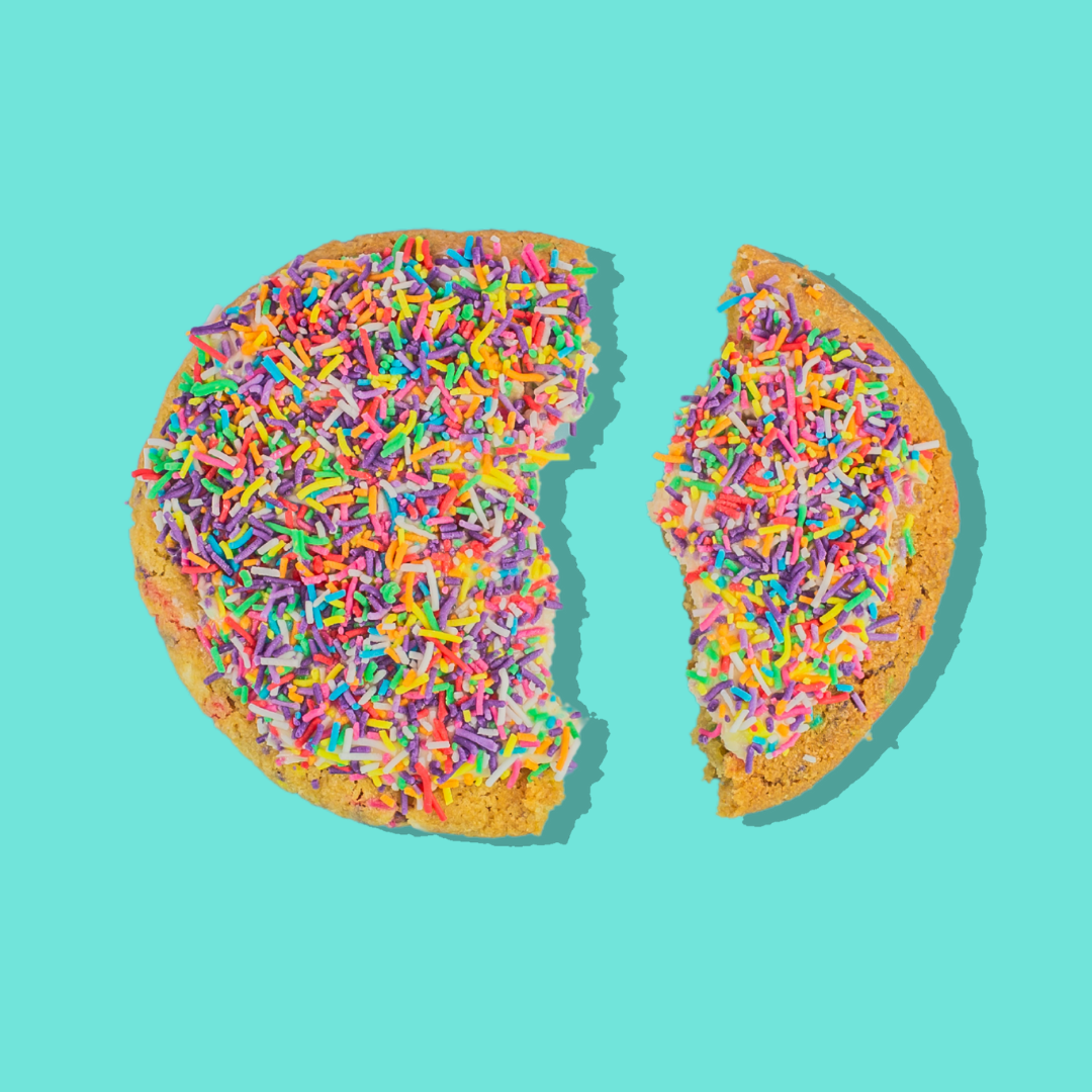 Cake Batter Maxi cookie with rainbow sprinkles and cake batter cream cheese frosting on blue background.