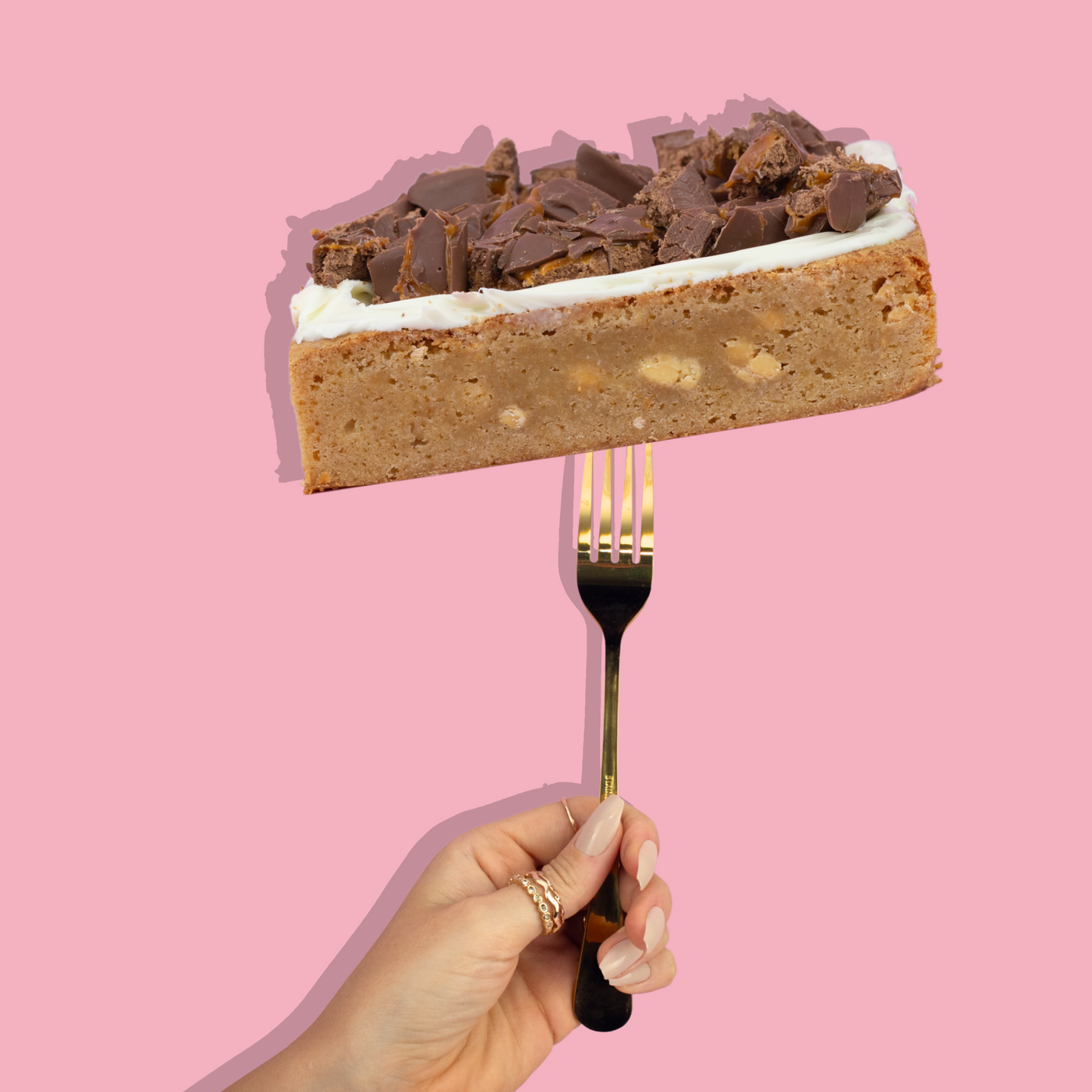 Loaded Blondie with chocolate topping on a fork against a pink background.