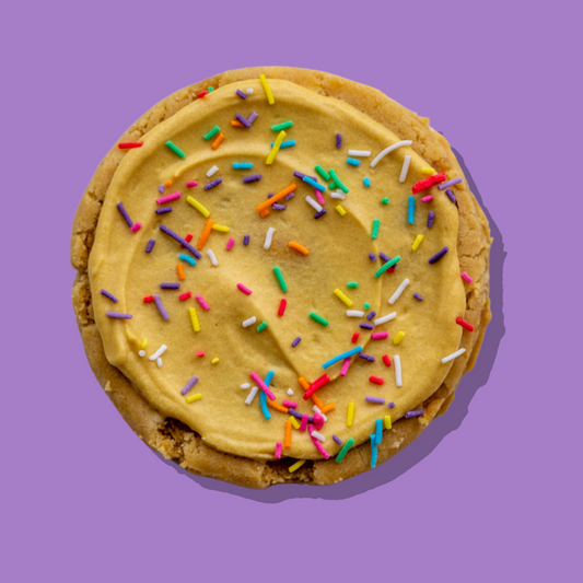 Caramel Donut Maxi with caramel-infused cream cheese frosting and rainbow sprinkles on purple background.