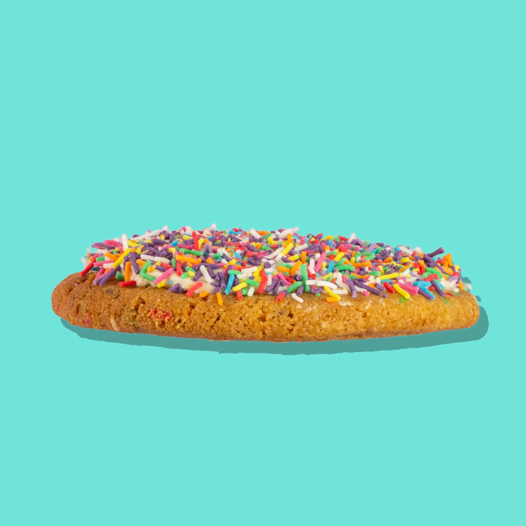 Cake Batter Maxi cookie with rainbow sprinkles and white chocolate chips on a turquoise background.
