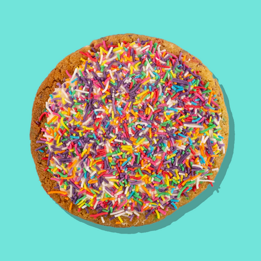 Cake Batter Maxi cookie with rainbow sprinkles and creamy frosting on a turquoise background.