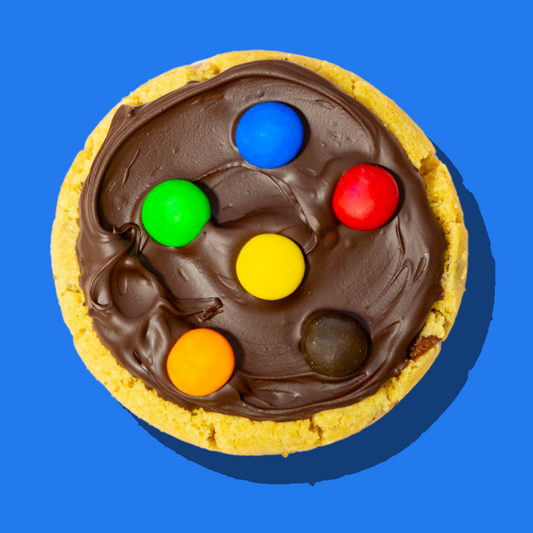 M&M Maxi cookie with milk chocolate ganache and colorful M&M toppings on a vibrant blue background.