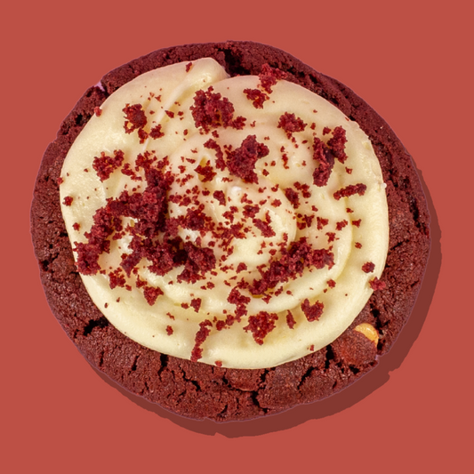 Red velvet cookie with white chocolate base, cream cheese frosting, and red velvet crumbs.
